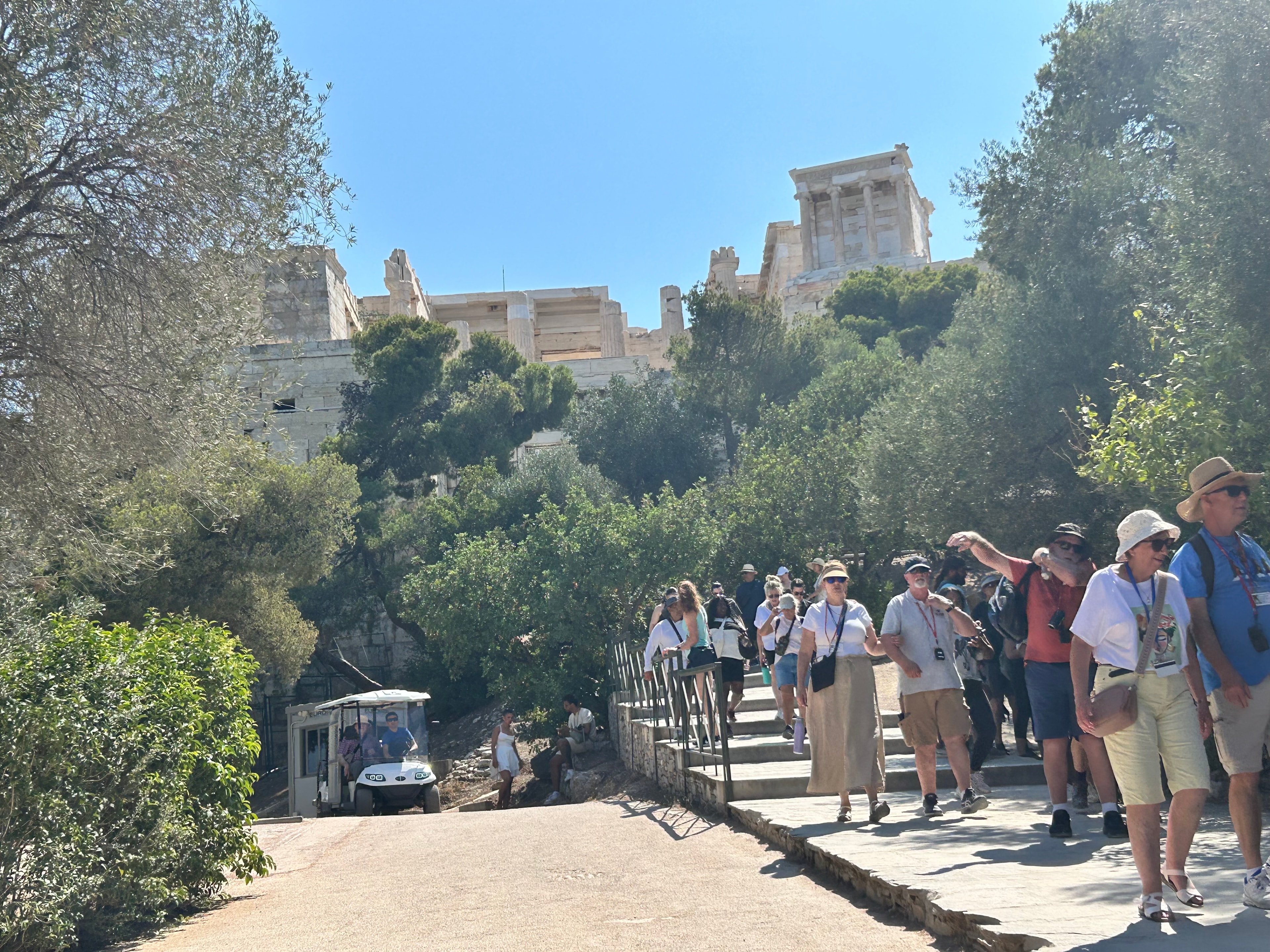Tourists and a golf cart at the base of the Acropolis — the accessible transport service